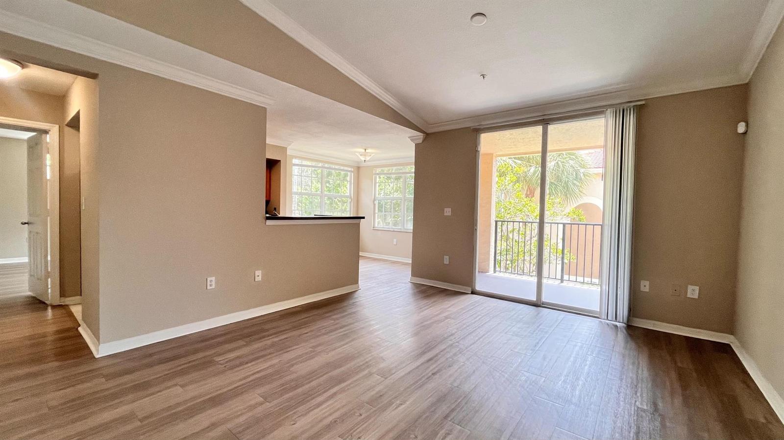 An interior view of a living room with wood-look flooring, beige walls, and a balcony — 15035 Michelangelo 202 Boulevard # 202, Delray Beach FL 33446, DELRAY BEACH, FL