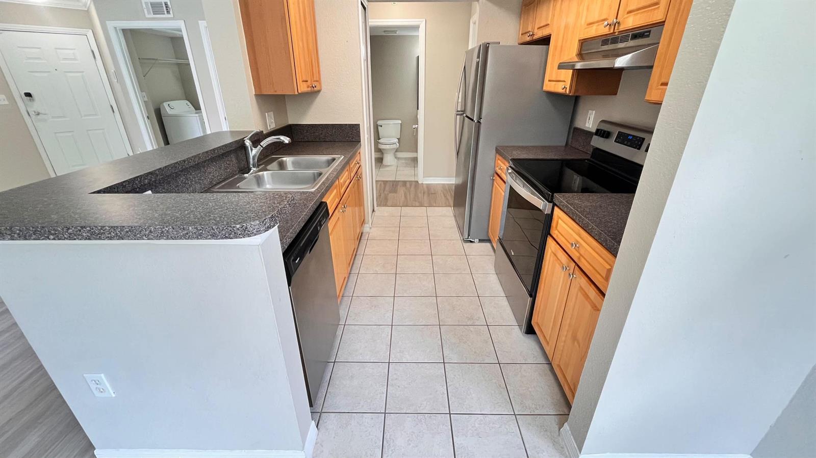 A galley-style kitchen features light wood cabinets, dark countertops, and stainless steel appliances — 15035 Michelangelo 202 Boulevard # 202, Delray Beach FL 33446, DELRAY BEACH, FL