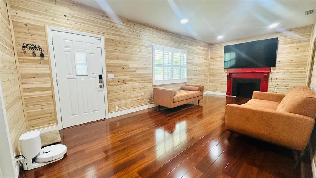 A living room features wood-paneled walls, hardwood floors, a red fireplace, and two orange sofas — 6804 BARRY ROAD, TAMPA, FL