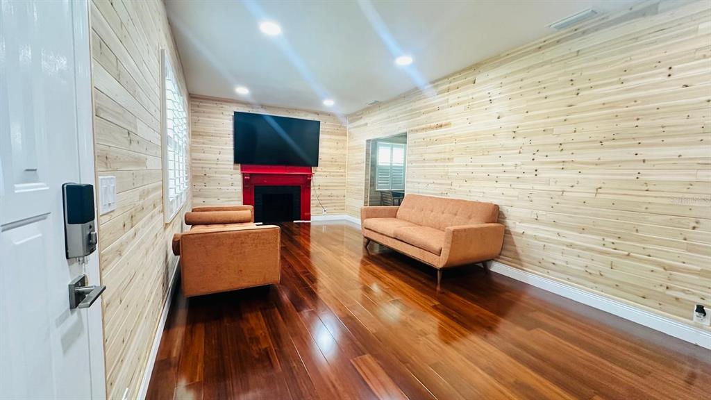 A living room features wood-paneled walls, a red fireplace, and a sofa on hardwood floors — 6804 BARRY ROAD, TAMPA, FL
