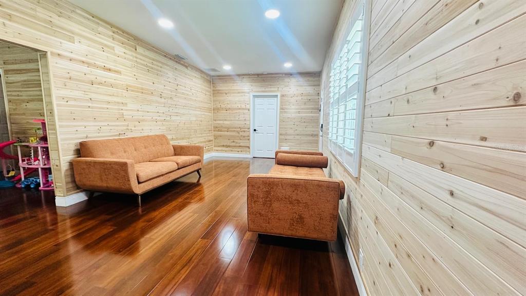 A living room features wood-paneled walls, dark hardwood floors, and two orange sofas — 6804 BARRY ROAD, TAMPA, FL