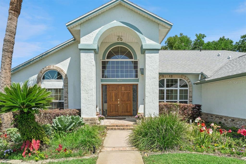 A light-colored house exterior features a covered entryway with double wooden doors and arched windows — 908 ALMOND TREE CIRCLE, ORLANDO, FL