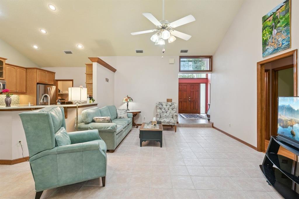 A living room with tile floors, a vaulted ceiling, and an open kitchen area — 908 ALMOND TREE CIRCLE, ORLANDO, FL