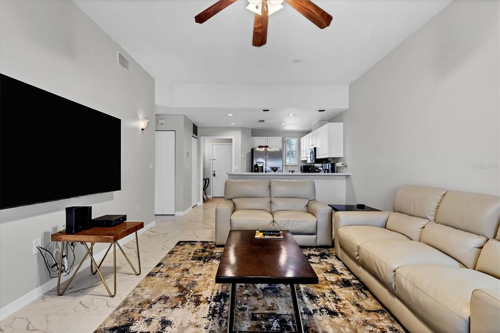 A living room features light-colored tile floors, a large television, and two beige leather sofas — 3706 54TH DRIVE W UNIT 102, BRADENTON, FL