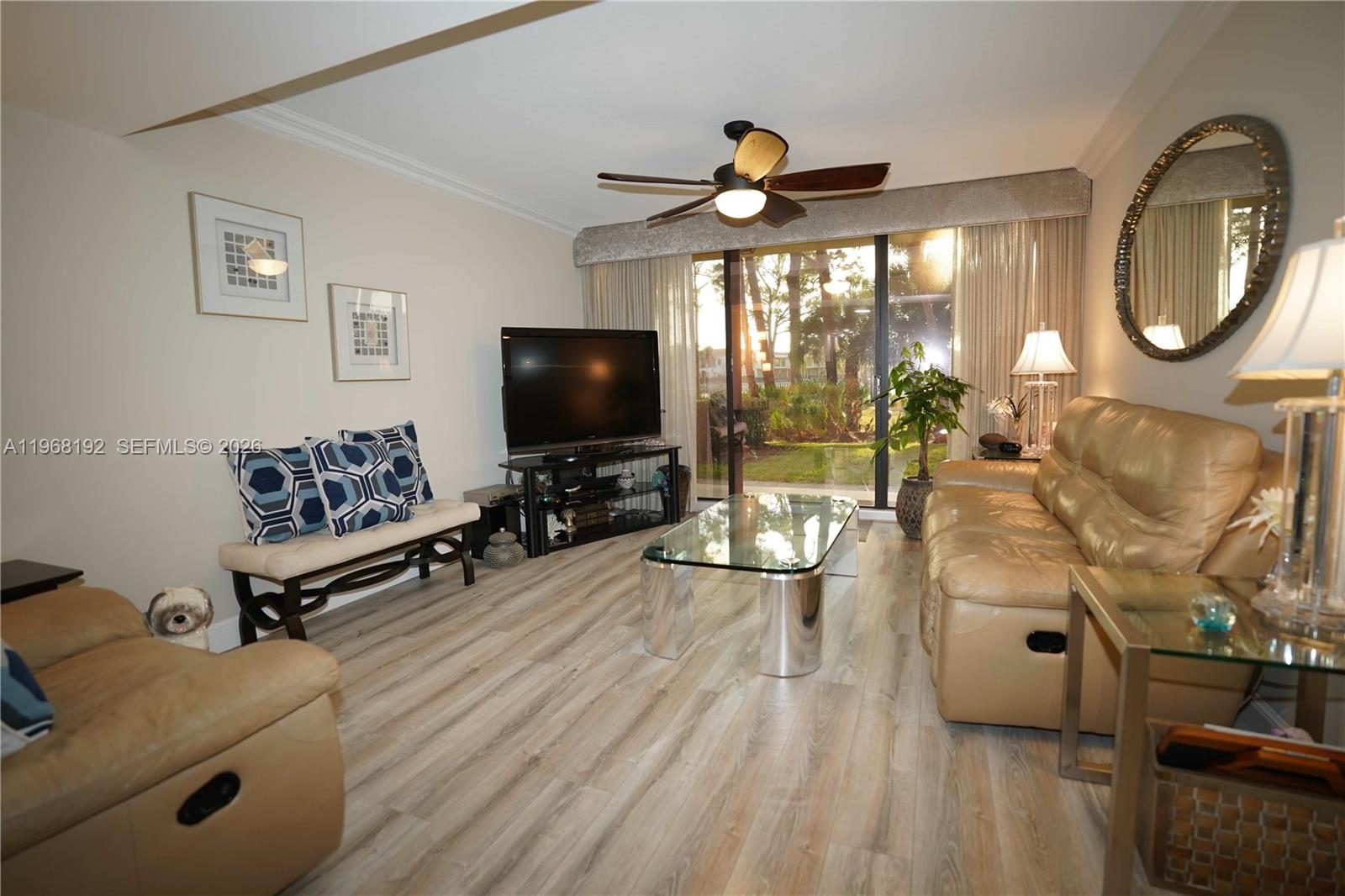 A living room features light wood flooring, a glass coffee table, and a leather sofa — 2101 Marina Isle Way # 104, Jupiter FL 33477, JUPITER, FL