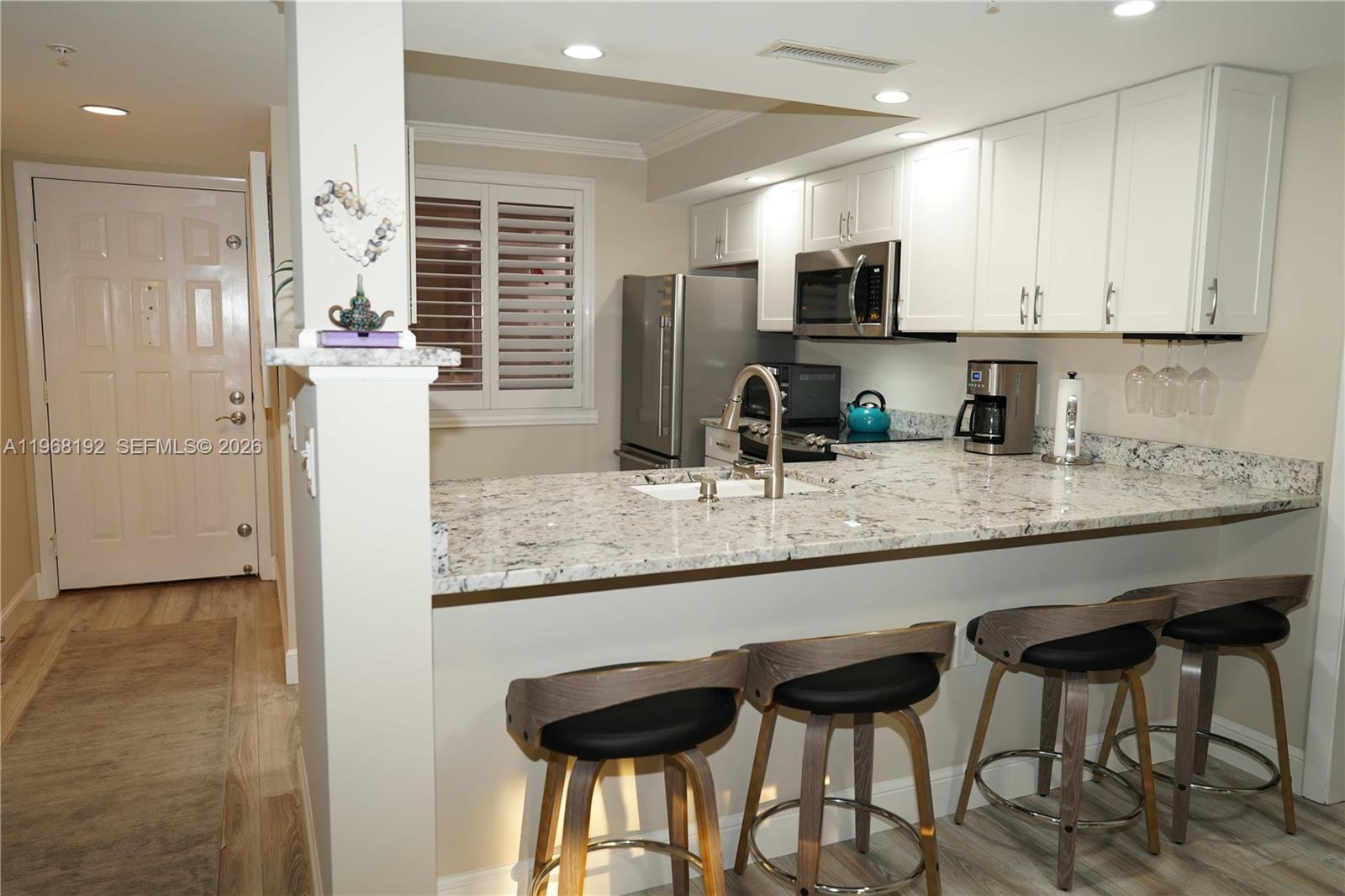 A kitchen features white cabinets, granite countertops, a breakfast bar with three stools, and stainless appliances — 2101 Marina Isle Way # 104, Jupiter FL 33477, JUPITER, FL