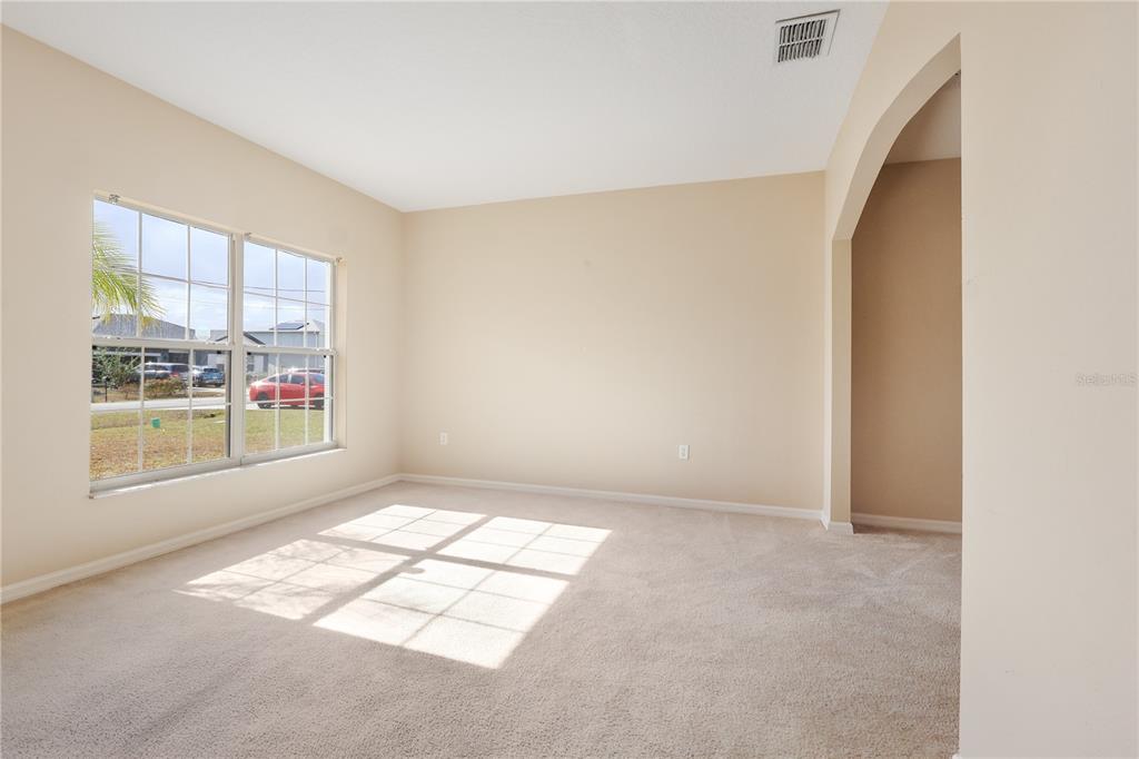 An empty room with beige walls, tan carpeting, and a window overlooking a residential street — 196 ATHABASCA DRIVE, POINCIANA, FL
