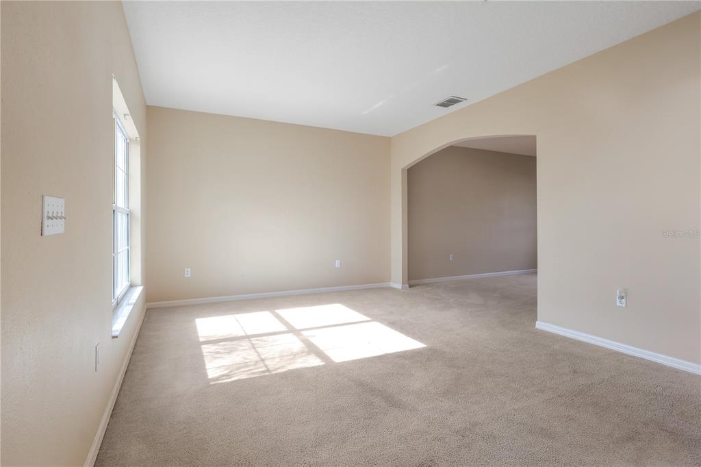 A carpeted living room features beige walls, a large window, and an arched entryway — 196 ATHABASCA DRIVE, POINCIANA, FL