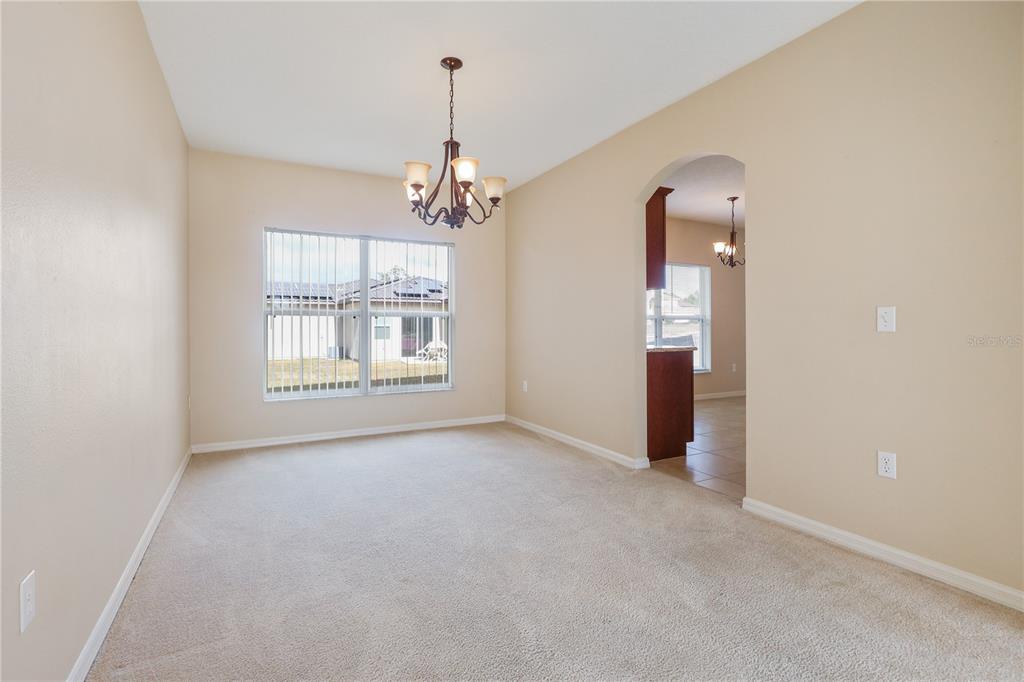 A carpeted dining room features a chandelier, a large window, and an arched entryway — 196 ATHABASCA DRIVE, POINCIANA, FL