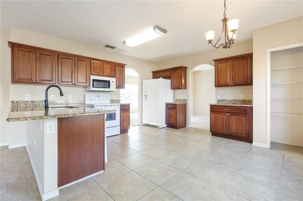 A kitchen with wood cabinets, granite countertops, tile flooring, and white appliances — 196 ATHABASCA DRIVE, POINCIANA, FL