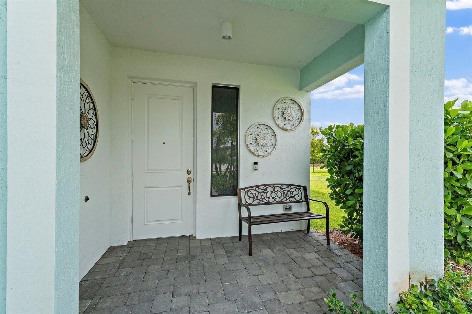 A covered front porch features a white door, a metal bench, and decorative wall art — 16378 Sea Turtle Place, Westlake FL 33470, WESTLAKE, FL