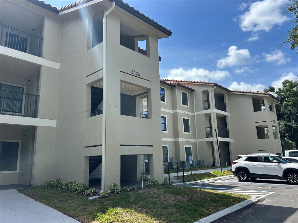 A multi-story apartment building with beige stucco walls and a tiled roof — 3024 PARKWAY BLVD UNIT 203, KISSIMMEE, FL