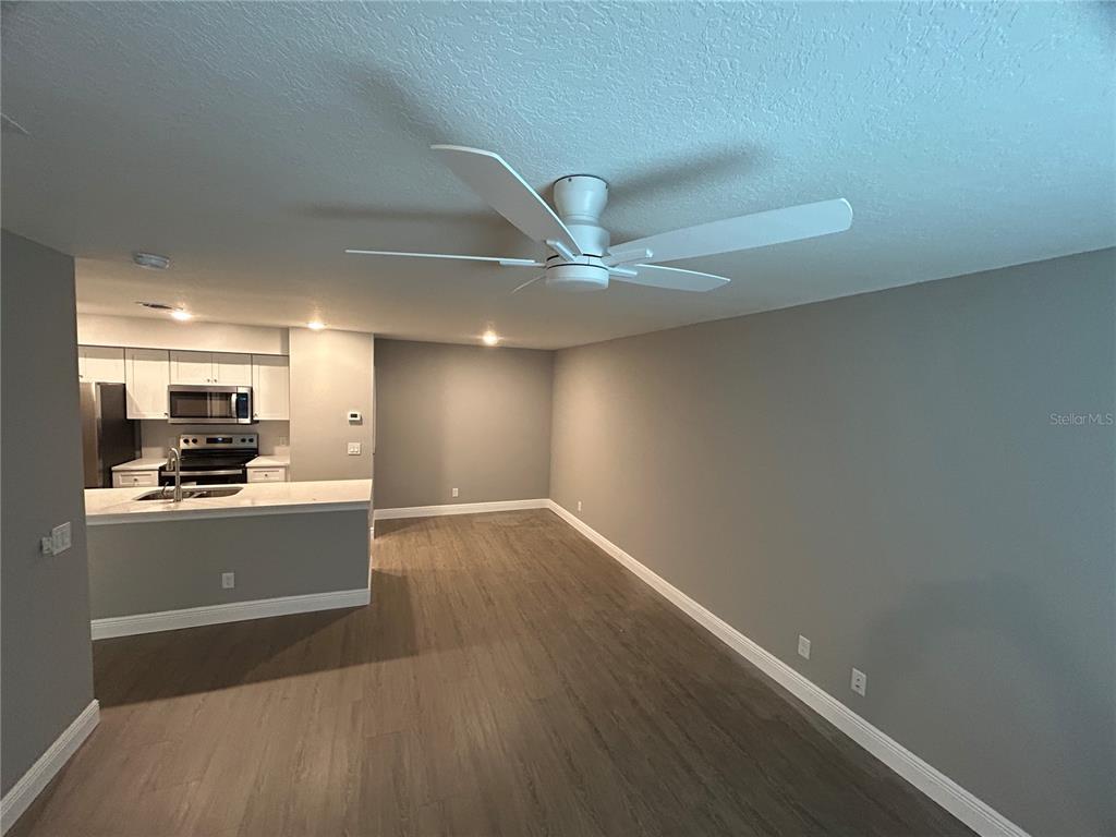An open-concept living area with gray walls, wood-look flooring, and an adjacent kitchen — 3024 PARKWAY BLVD UNIT 203, KISSIMMEE, FL