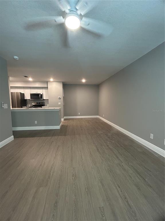 An open-concept living area with gray walls, wood-look flooring, and a kitchen with white cabinets — 3024 PARKWAY BLVD UNIT 203, KISSIMMEE, FL