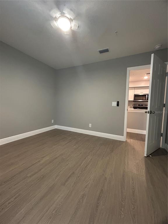 An empty room with gray walls, wood-look flooring, and a doorway leading to a kitchen — 3024 PARKWAY BLVD UNIT 203, KISSIMMEE, FL