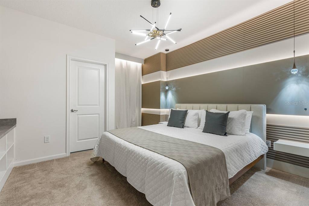 A bedroom features a bed with a grey runner, a modern chandelier, and slatted wall panels — 5943 HIGH SEAS DRIVE, ORLANDO, FL
