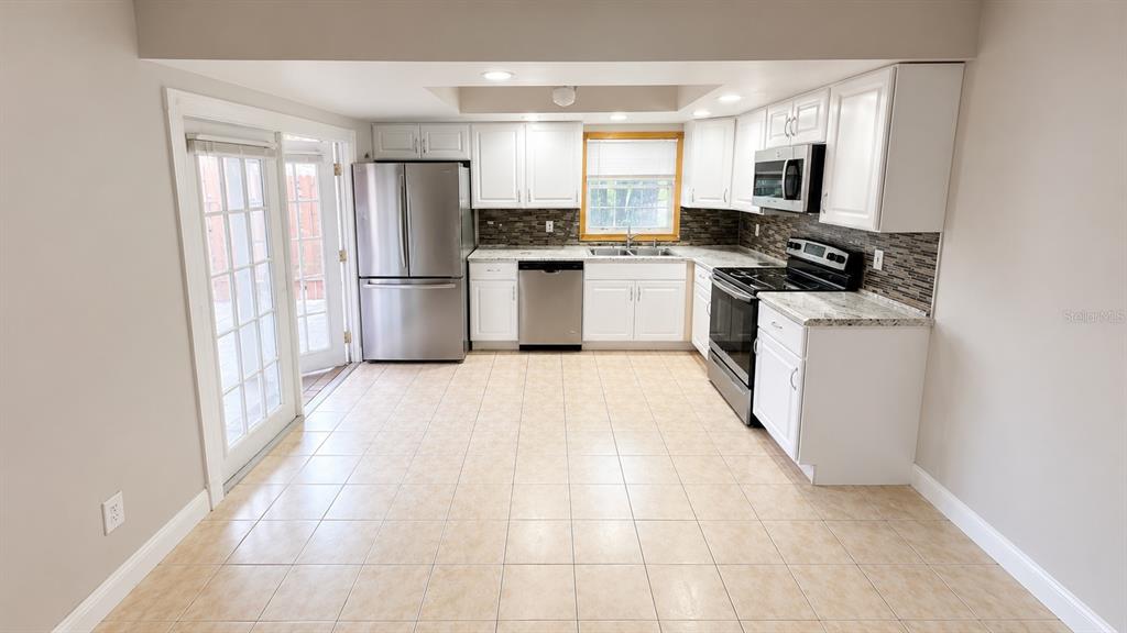A kitchen with white cabinets, stainless steel appliances, tile flooring, and a glass door — 120 MOONSTONE COURT, PORT ORANGE, FL