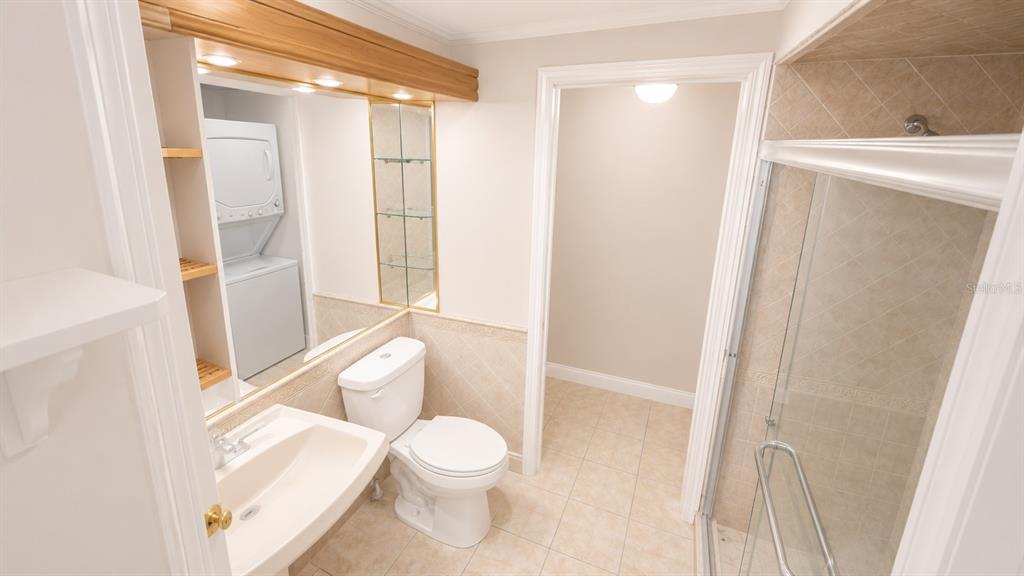 A bathroom features a pedestal sink, toilet, glass-enclosed shower, and a stacked washer and dryer — 120 MOONSTONE COURT, PORT ORANGE, FL