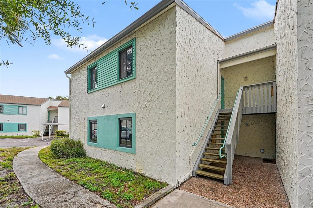A two-story stucco apartment building with teal window trim and a concrete walkway — 11502 7TH LANE N UNIT 1401, ST PETERSBURG, FL