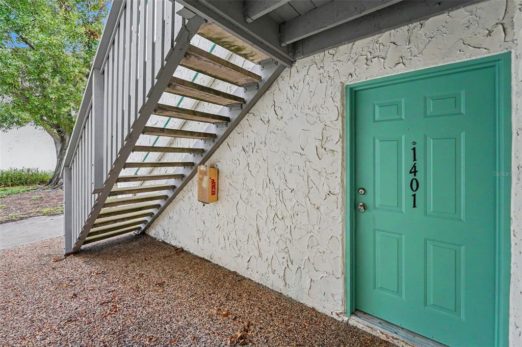 A teal front door with the number 1401 is located beneath an outdoor wooden staircase — 11502 7TH LANE N UNIT 1401, ST PETERSBURG, FL