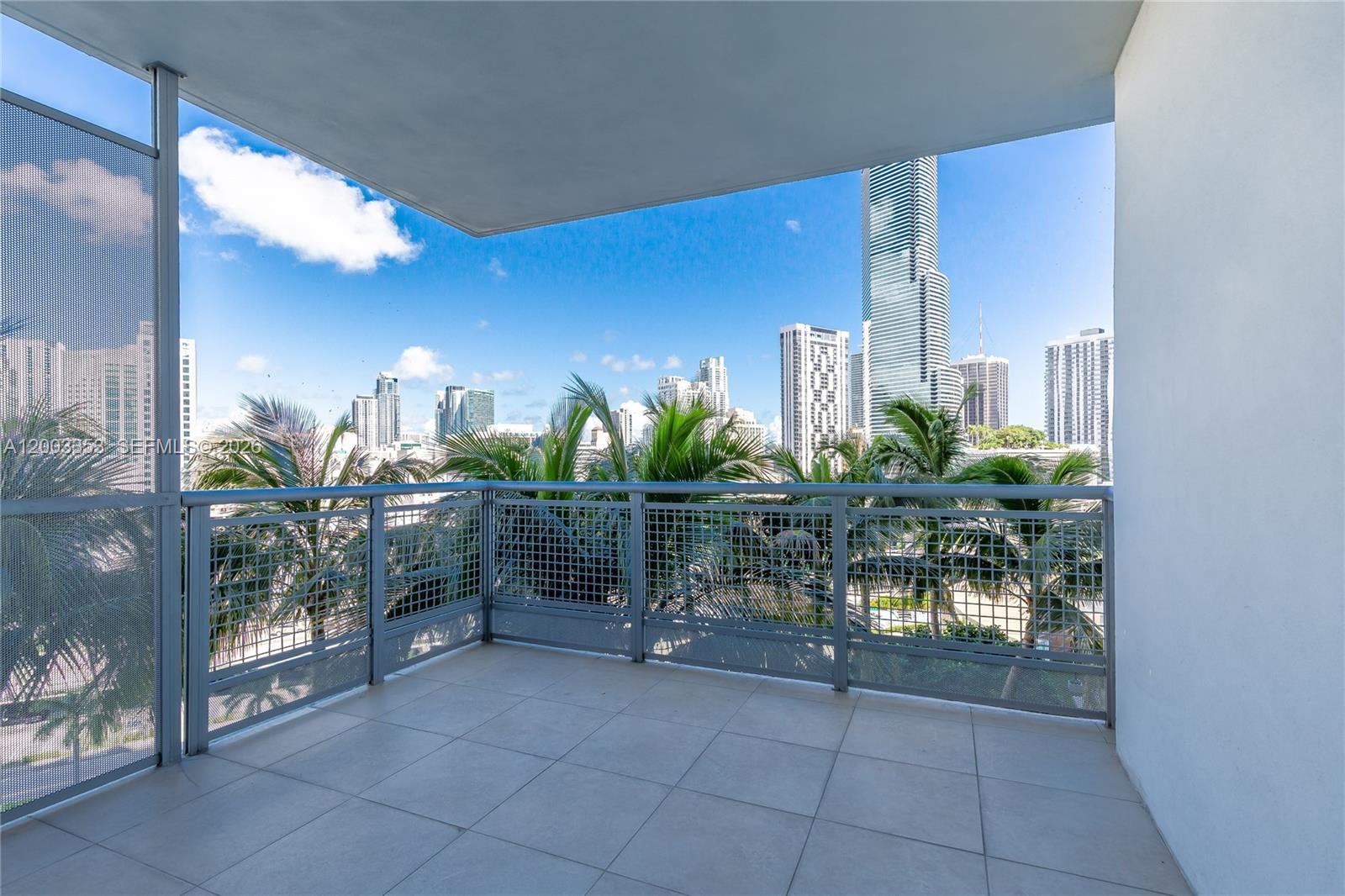 A balcony with tiled flooring and metal railings overlooks a city skyline with palm trees — 350 S Miami Ave # 1207, Miami FL 33130, MIAMI, FL