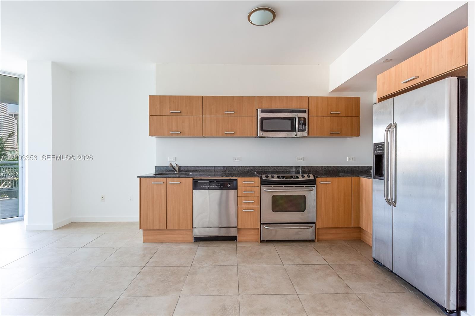 A kitchen features light wood cabinets, stainless steel appliances, and dark countertops on tile flooring — 350 S Miami Ave # 1207, Miami FL 33130, MIAMI, FL