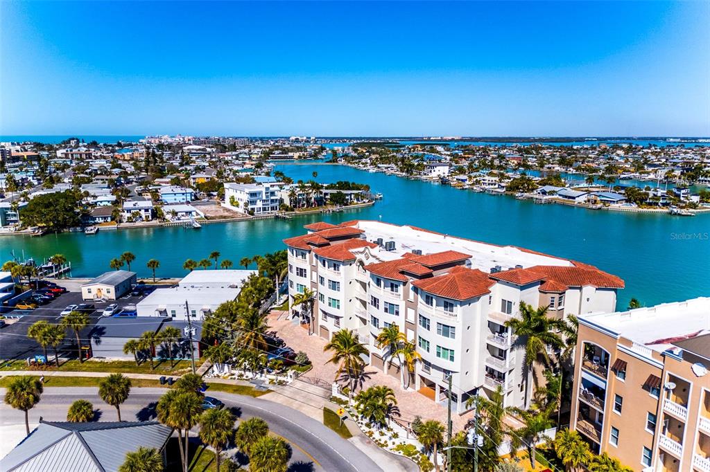 An aerial view shows a multi-story apartment building situated along a canal near the coast — 220 108TH AVENUE UNIT 304, TREASURE ISLAND, FL