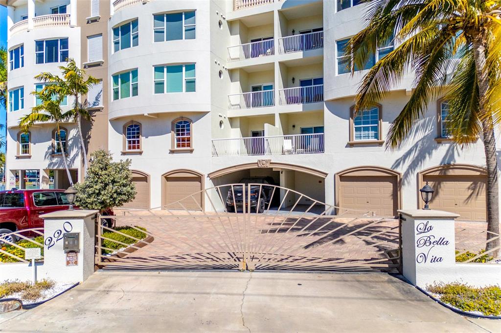 A gated entrance leads to a multi-story residential building with garages and balconies — 220 108TH AVENUE UNIT 304, TREASURE ISLAND, FL