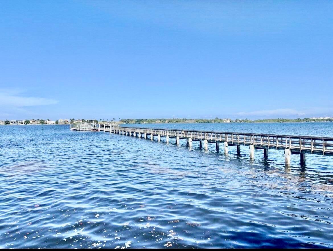 A long wooden pier extends over calm blue water toward a distant shoreline — 621 Windward Circle S, Boynton Beach FL 33435, BOYNTON BEACH, FL