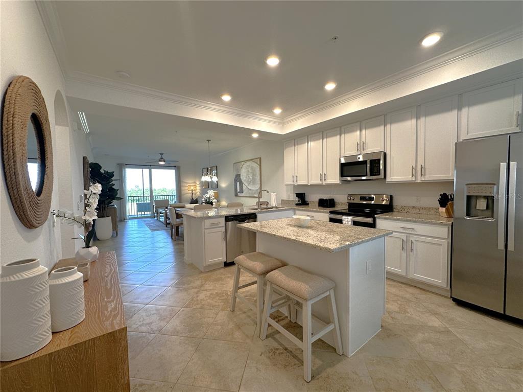 A kitchen with white cabinets, granite countertops, and a center island with two stools — 14071 HERITAGE LANDING BOULEVARD UNIT 325, PUNTA GORDA, FL