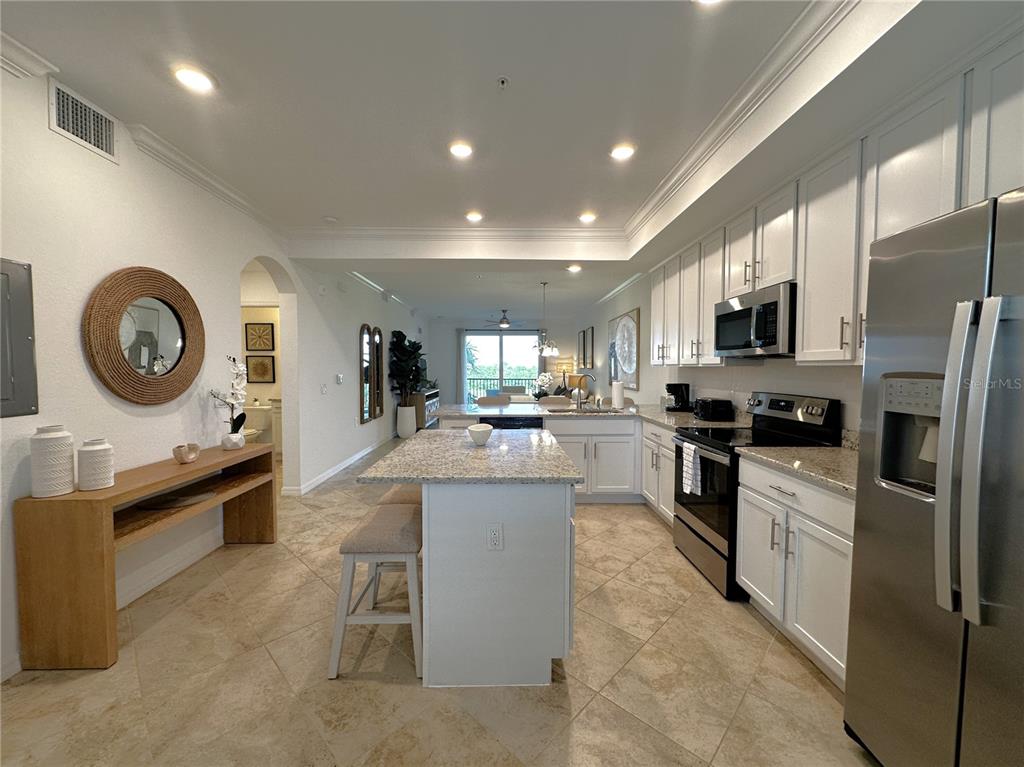 A kitchen with white cabinets, granite countertops, and a central island opens to a living area — 14071 HERITAGE LANDING BOULEVARD UNIT 325, PUNTA GORDA, FL