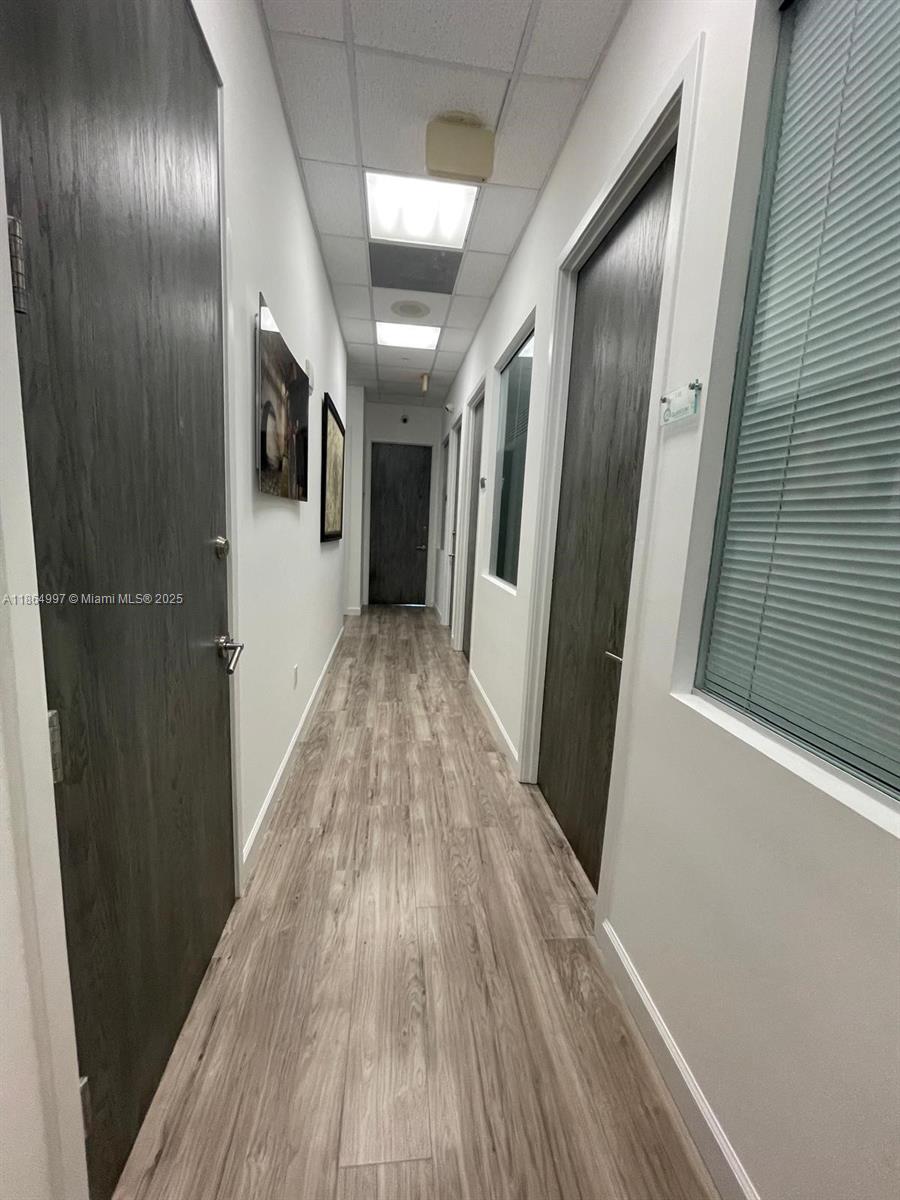 A narrow office hallway features wood-look flooring, dark doors, and recessed ceiling lighting — 1900 N Bayshore Dr # 1A, Miami FL 33132, MIAMI, FL