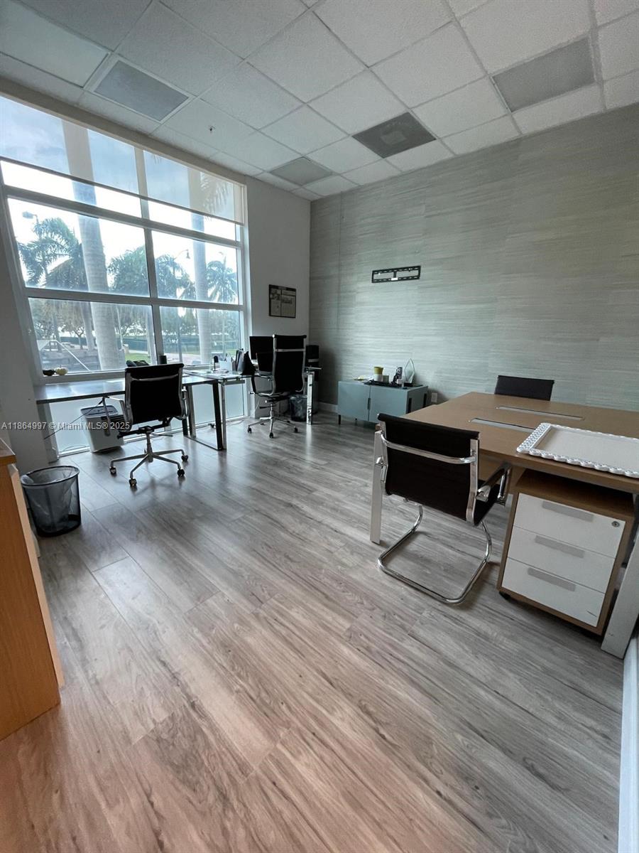 An office features wood-look flooring, a large window, and multiple desks with chairs — 1900 N Bayshore Dr # 1A, Miami FL 33132, MIAMI, FL