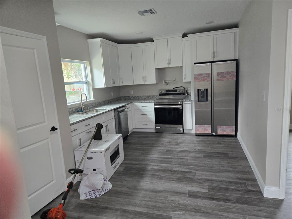 A kitchen features white cabinets, stainless steel appliances, granite countertops, and gray wood-look flooring — 701 E LINEBAUGH AVENUE, TAMPA, FL