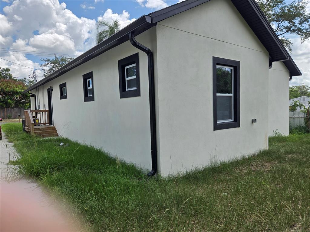 The exterior of a light-colored house features dark trim, black gutters, and a wooden deck — 701 E LINEBAUGH AVENUE, TAMPA, FL