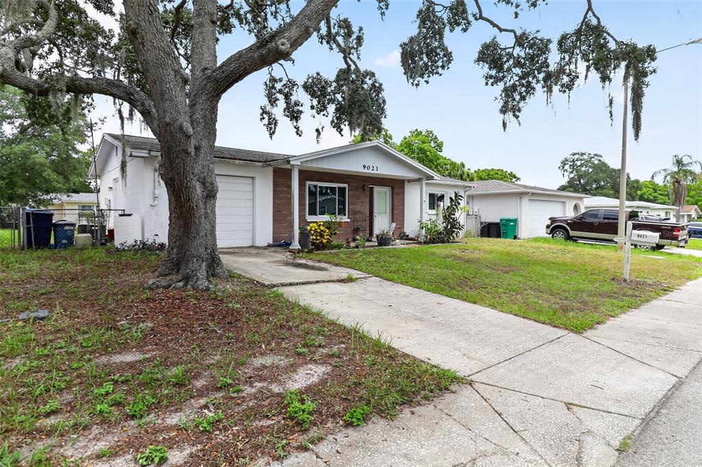 A single-story house with a brick facade, a concrete driveway, and a large oak tree — 9021 RICHWOOD LANE, PORT RICHEY, FL