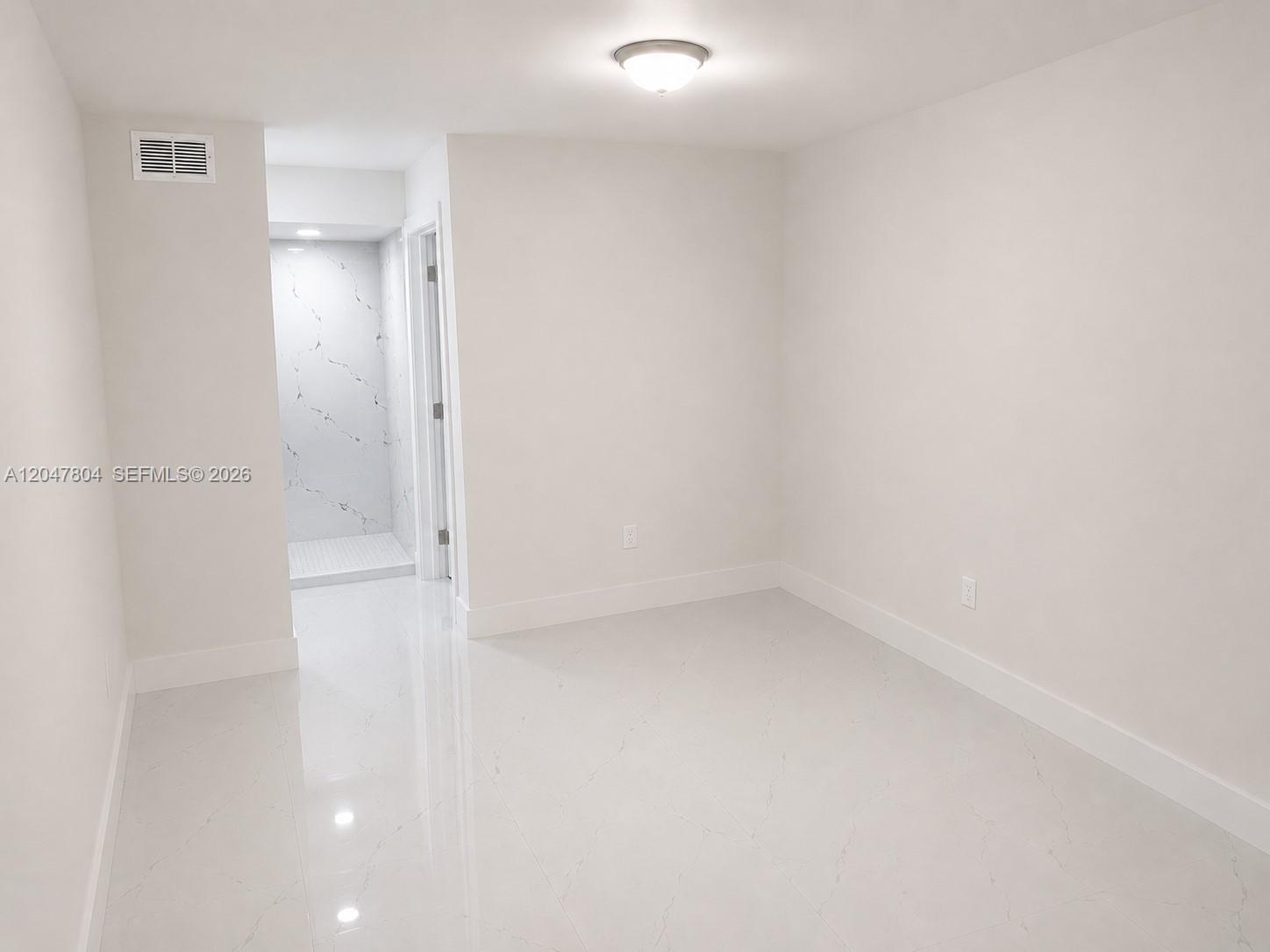 A bright, minimalist room features white tile flooring and a doorway leading to a shower — 479 NE 210th Cir Ter # 28, Miami FL 33179, MIAMI, FL
