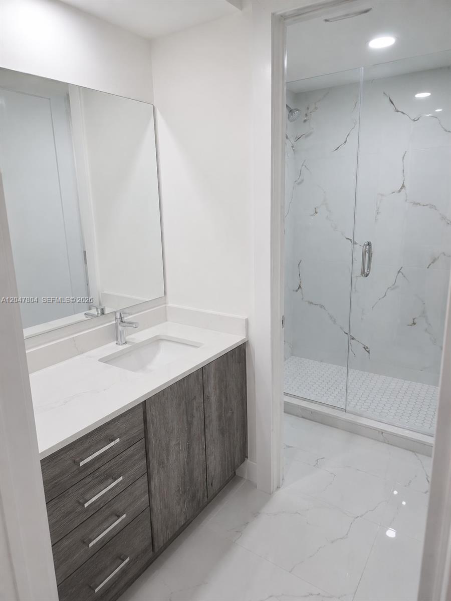 A modern bathroom features a gray wood vanity, white countertop, and a glass-enclosed shower — 479 NE 210th Cir Ter # 28, Miami FL 33179, MIAMI, FL