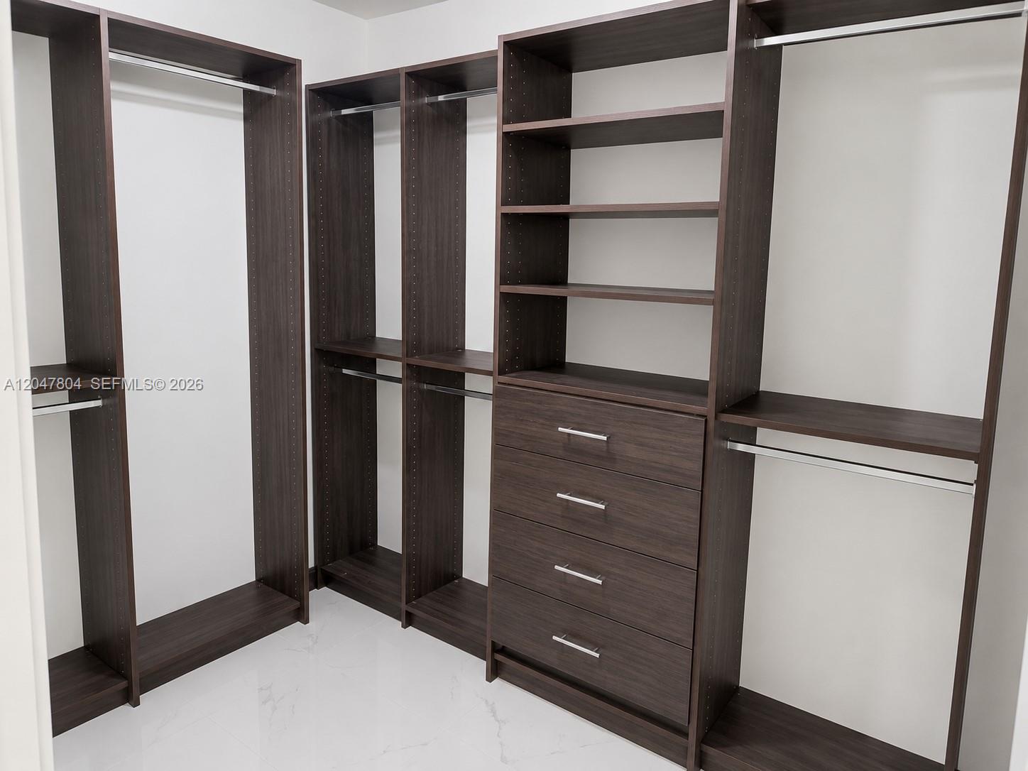 A walk-in closet features dark wood shelving, hanging rods, and a four-drawer dresser unit — 479 NE 210th Cir Ter # 28, Miami FL 33179, MIAMI, FL