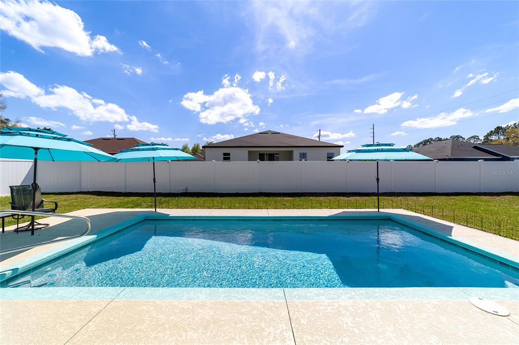 A backyard swimming pool with three blue umbrellas sits in front of a white fence — 4838 SW 130TH STREET, OCALA, FL
