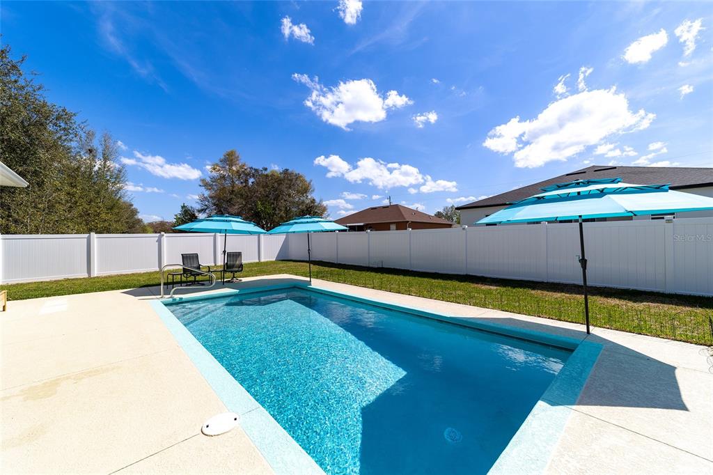 A rectangular swimming pool sits in a backyard enclosed by a white vinyl fence — 4838 SW 130TH STREET, OCALA, FL