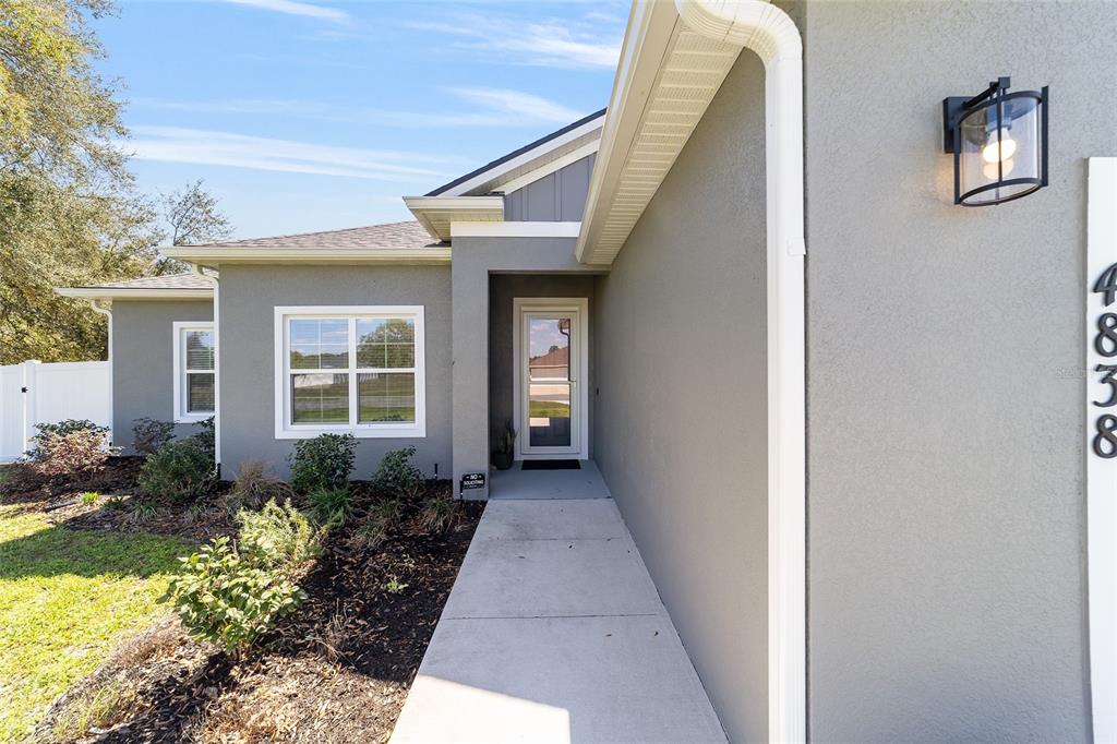 The exterior of a gray house features a concrete walkway leading to the front door — 4838 SW 130TH STREET, OCALA, FL
