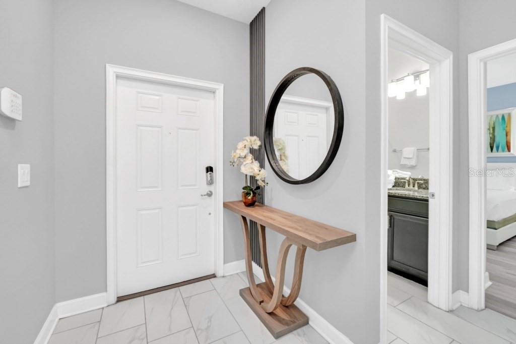 A modern entryway features a white door, a wood console table, and a round mirror — 4876 ROMEO CIRCLE, KISSIMMEE, FL