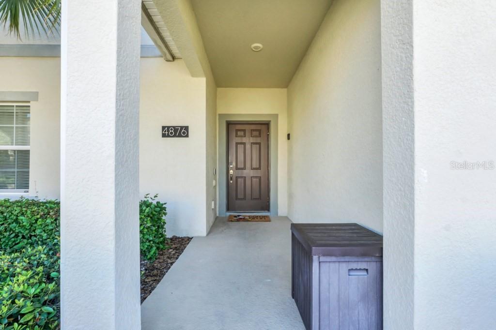A covered entryway features a brown front door, a house number, and a storage bin — 4876 ROMEO CIRCLE, KISSIMMEE, FL