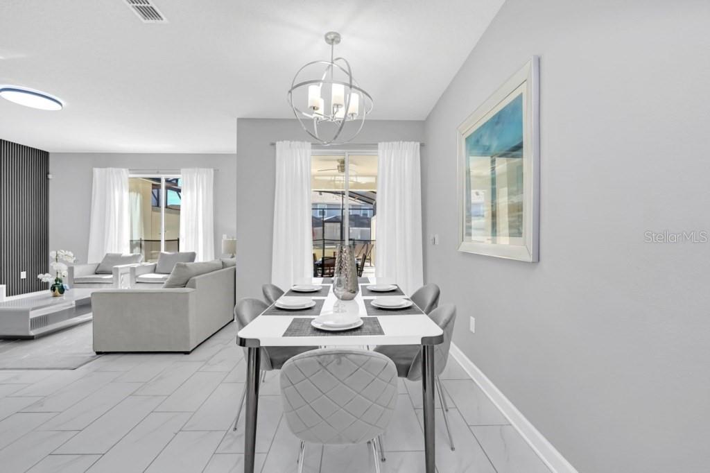 A dining area with a modern chandelier, white table, and grey chairs opens to a patio — 4876 ROMEO CIRCLE, KISSIMMEE, FL