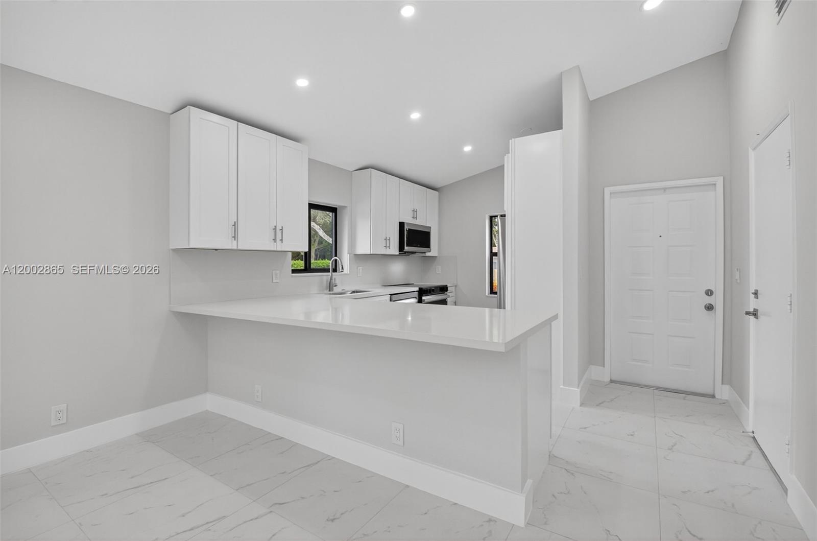 A modern kitchen features white cabinets, a quartz breakfast bar, and light-colored tile flooring — 8067 Summerbreeze Ln, Boca Raton FL 33496, BOCA RATON, FL
