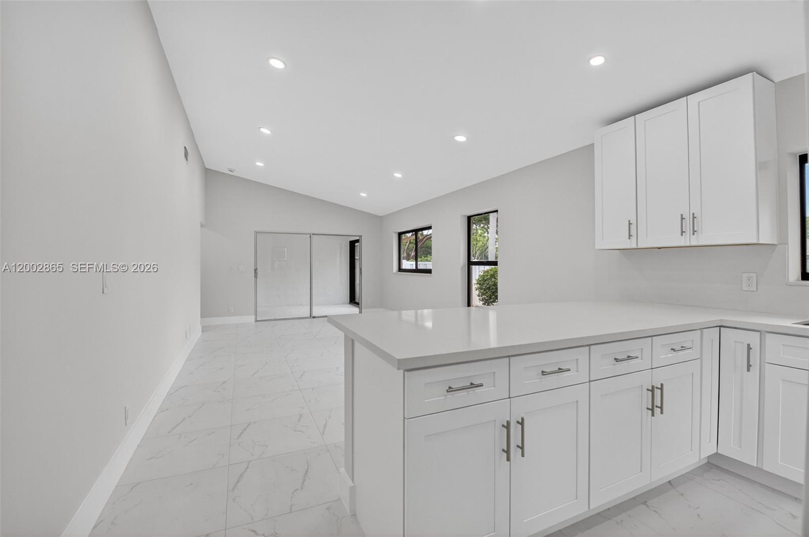 A modern kitchen with white cabinets and quartz countertops overlooks an open living area — 8067 Summerbreeze Ln, Boca Raton FL 33496, BOCA RATON, FL