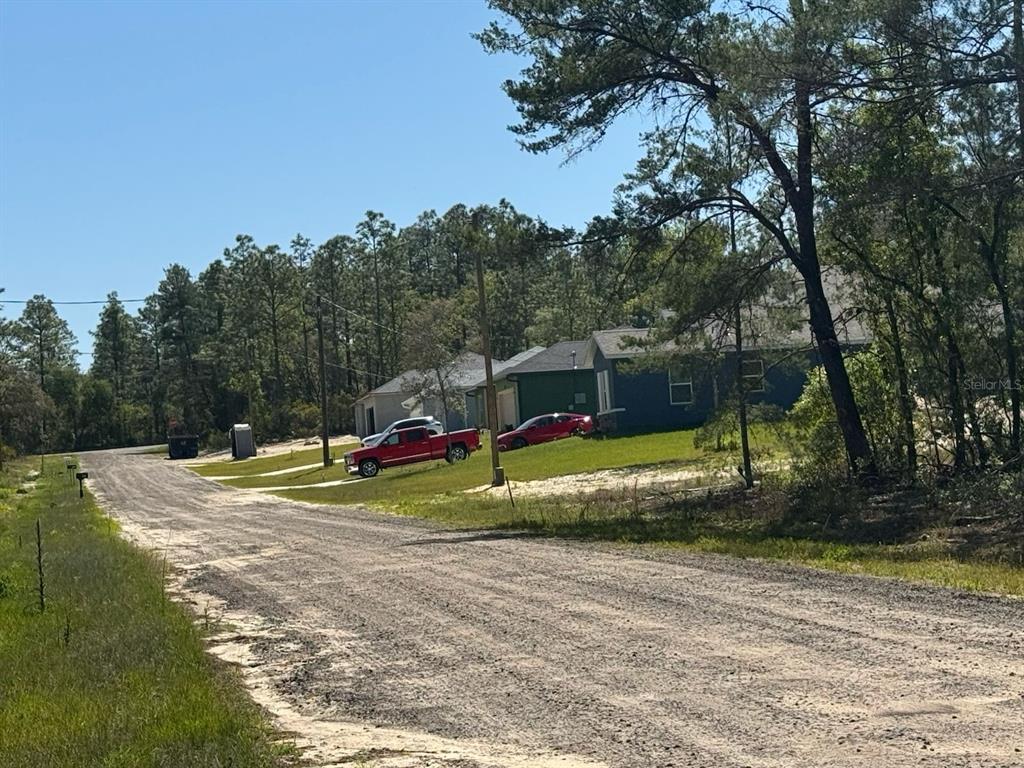 A dirt road leads toward houses surrounded by trees under a clear blue sky — 3861 W MALBY LANE, DUNNELLON, FL