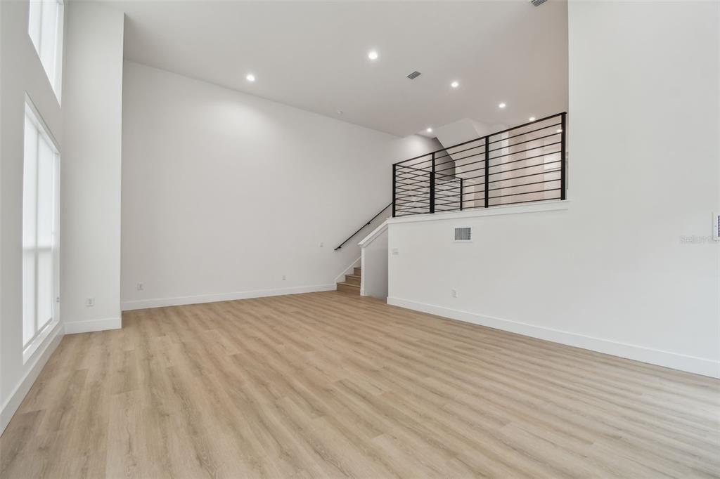 An empty room with high ceilings, light wood-look flooring, and a staircase with metal railings — 3826 POMPANO DRIVE SE, ST PETERSBURG, FL