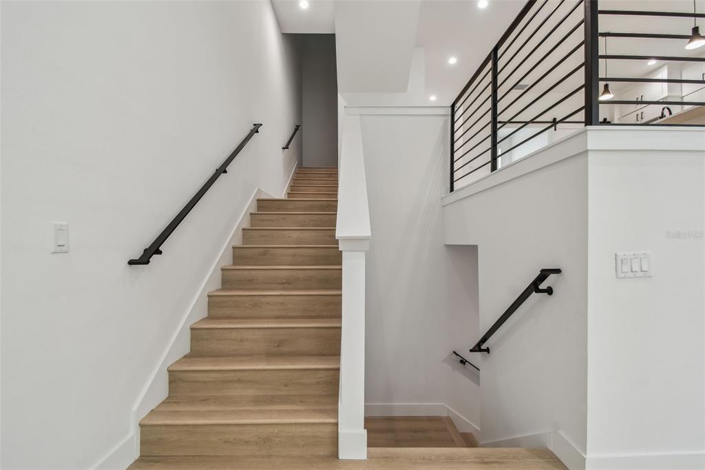 A staircase with light wood treads and black railings leads to an upper landing — 3826 POMPANO DRIVE SE, ST PETERSBURG, FL